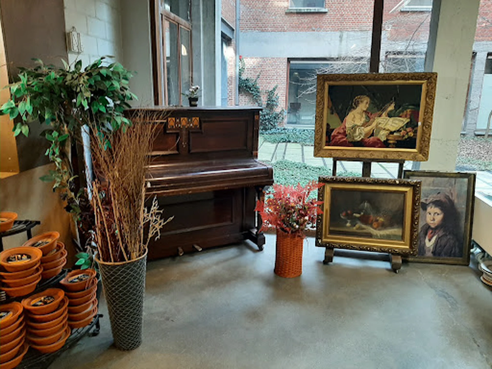 Winkelbinnenruimte met vleugelpiano, schilderijen op ezel, plantjes, oranje schalen en vintage decorstukken