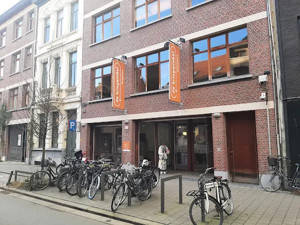 Bakstenen gevel van kringloopwinkel met grote ramen, oranje decoratieve elementen en fietsen geparkeerd voor de deur
