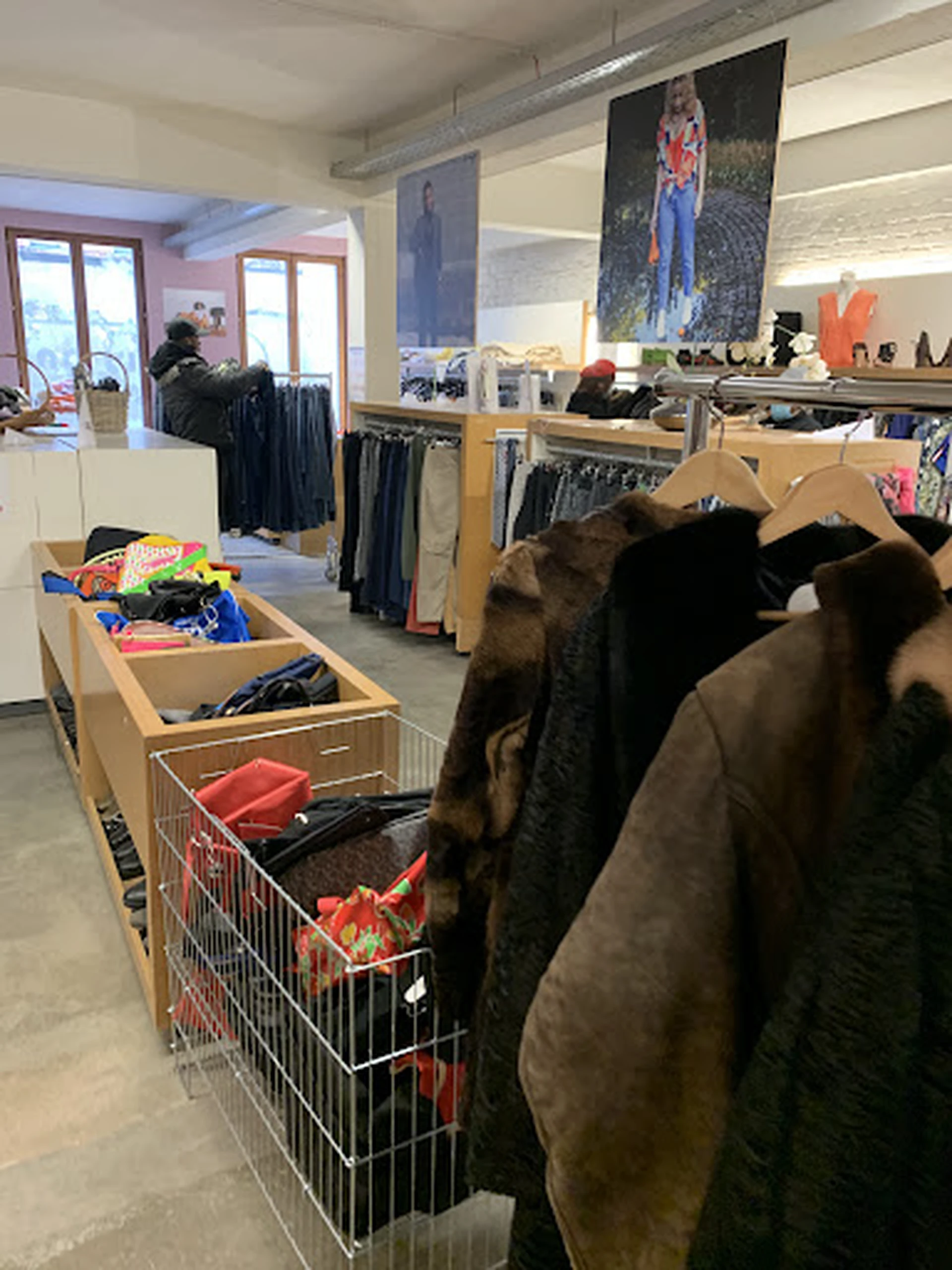Rekken met tweedehands kleding, waaronder jassen en uitgestalde artikelen in bakken op de winkelvloer