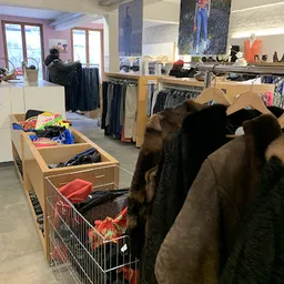 Rekken met tweedehands kleding, waaronder jassen en uitgestalde artikelen in bakken op de winkelvloer