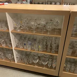 Glazenkast met diverse glaswerk en serviesgoed netjes uitgestald op houten planken