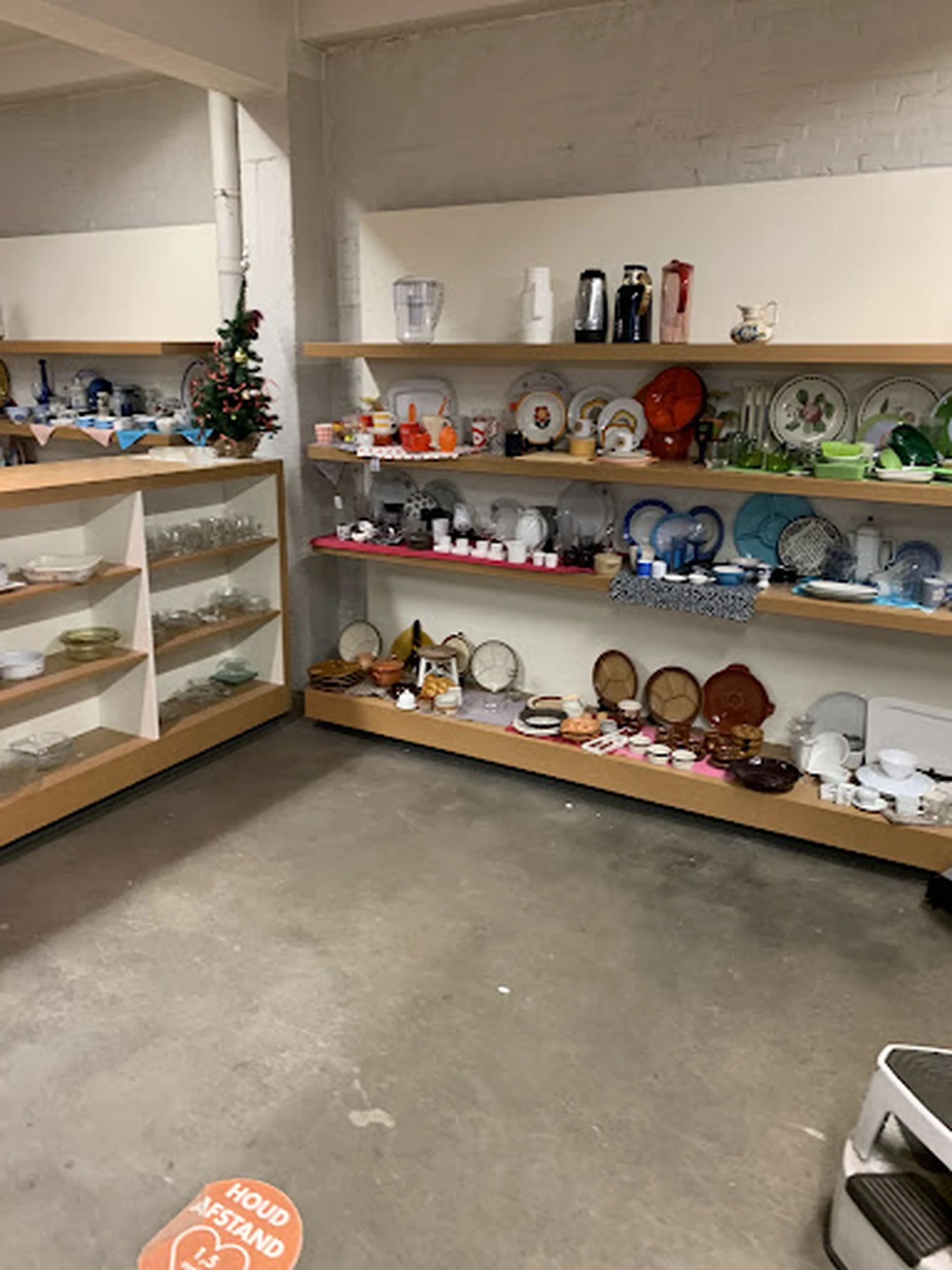 Houten stellingen met serviesgoed, borden, kopjes en huishoudelijke spullen in kringloopwinkel