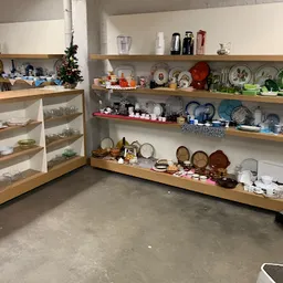 Houten stellingen met serviesgoed, borden, kopjes en huishoudelijke spullen in kringloopwinkel