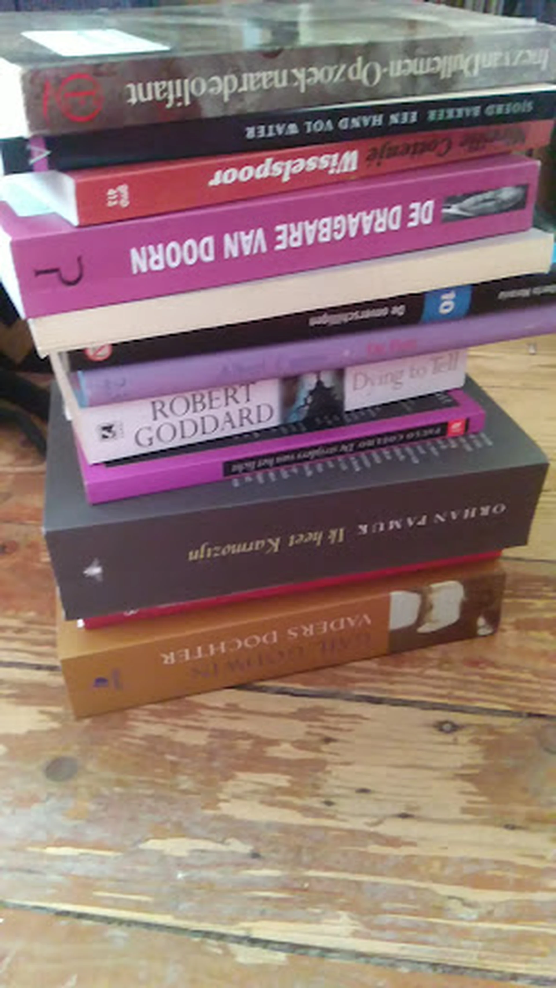 Stapel boeken met daarop onder meer een werk van Robert Goddard, op houten vloer