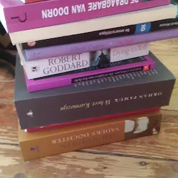 Stapel boeken met daarop onder meer een werk van Robert Goddard, op houten vloer