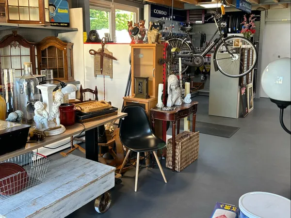 Winkelinterieur met diverse meubels, een fiets aan de muur, een zwarte stoel en dozen, sfeervolle kringloopwinkel