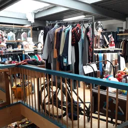 Winkelvloer met kledingrekken, stellingen en uitgestalde tweedehands kleding op meerdere niveaus