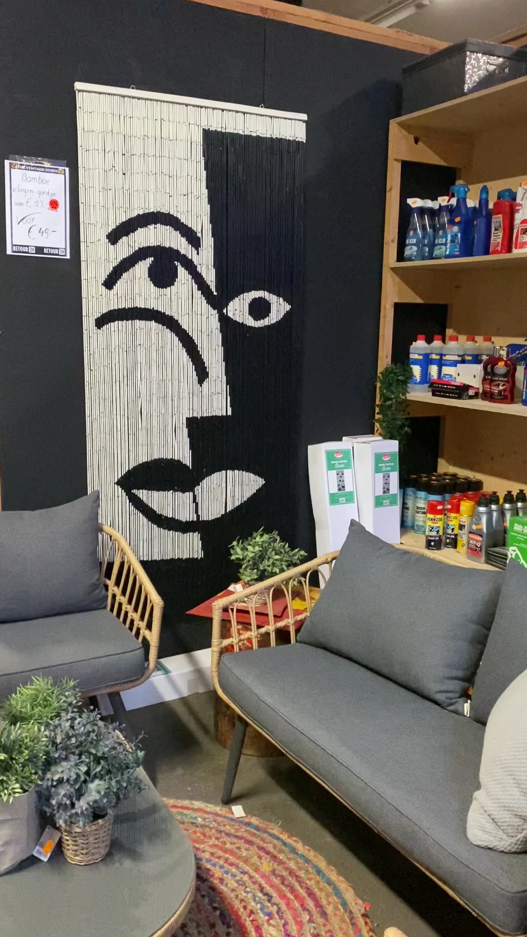 Winkelinterieur met grijze fauteuils, zwart-wit kunstwerk aan muur, houten plantenbak en houten planken met diverse producten