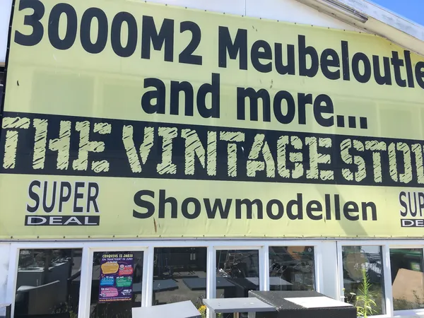 Gele gevel van The Vintage Store met text over meubeloutlet en showmodellen, winkelnaam zichtbaar