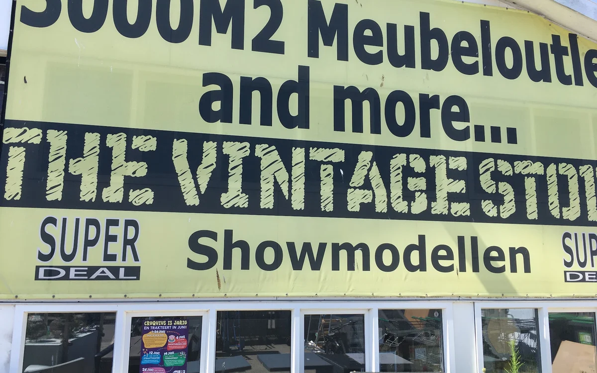 Gele gevel van The Vintage Store met text over meubeloutlet en showmodellen, winkelnaam zichtbaar