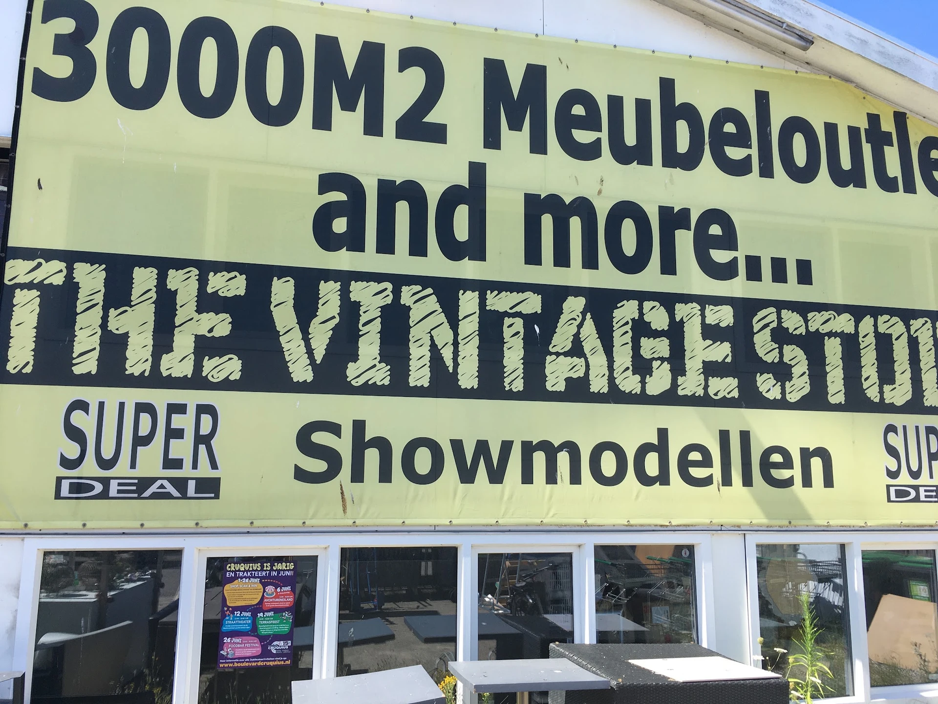 Gele gevel van The Vintage Store met text over meubeloutlet en showmodellen, winkelnaam zichtbaar