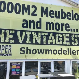 Gele gevel van The Vintage Store met text over meubeloutlet en showmodellen, winkelnaam zichtbaar