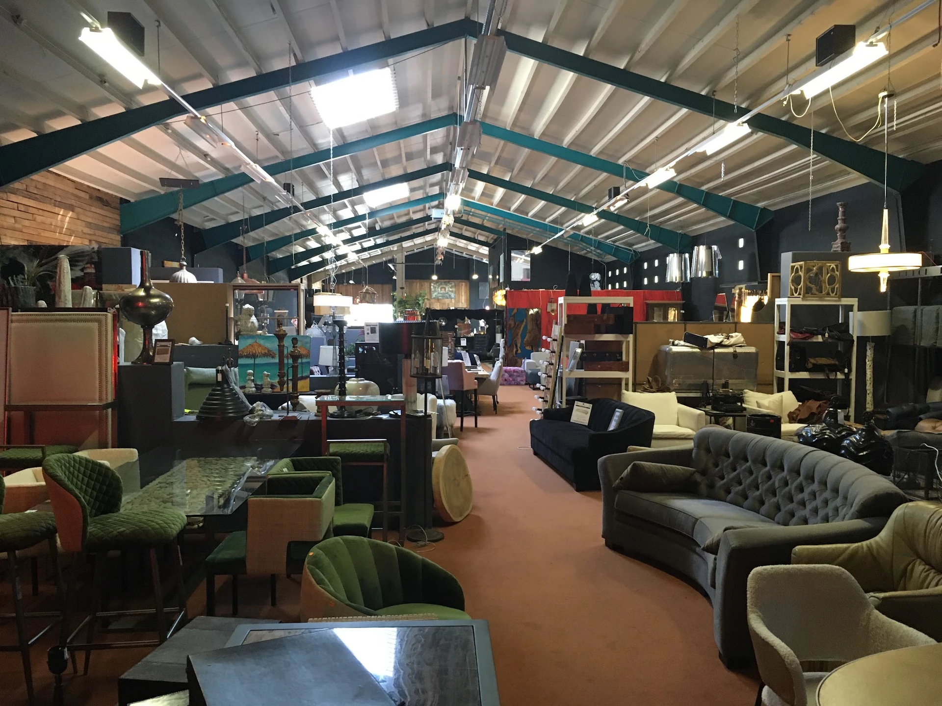 Ruim winkelsinterieur met vintage meubels, banken, stoelen en kasten onder industrieel plafond