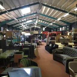 Ruim winkelsinterieur met vintage meubels, banken, stoelen en kasten onder industrieel plafond