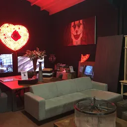Winkelinterieur met grijze bank, rode bureau, neonverlichting en houten kasten met diverse spullen