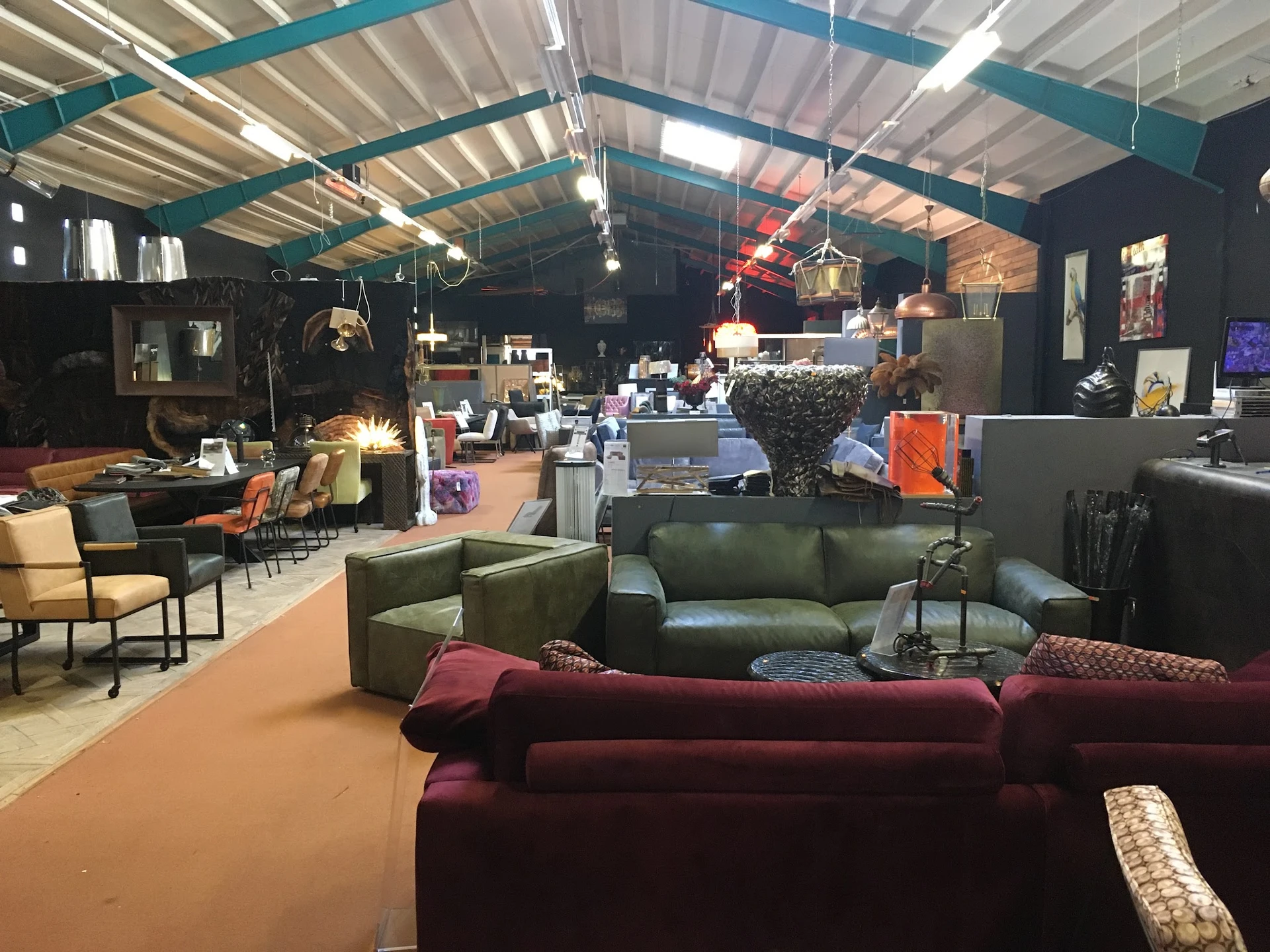 Ruim interieur van kringloopwinkel met meubels uitgestald, waaronder rode en groene zitmeubels op oranje vloer