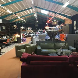 Ruim interieur van kringloopwinkel met meubels uitgestald, waaronder rode en groene zitmeubels op oranje vloer