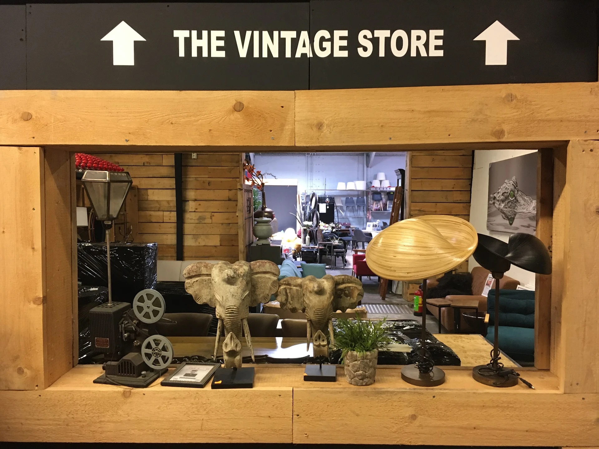 Vitrinekast met vintage decoratie: gouden olifanten, houten lamp, miniatuurauto's, plantenpotten en diverse andere antieke sp