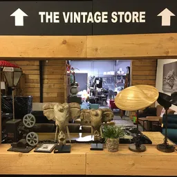 Vitrinekast met vintage decoratie: gouden olifanten, houten lamp, miniatuurauto's, plantenpotten en diverse andere antieke sp