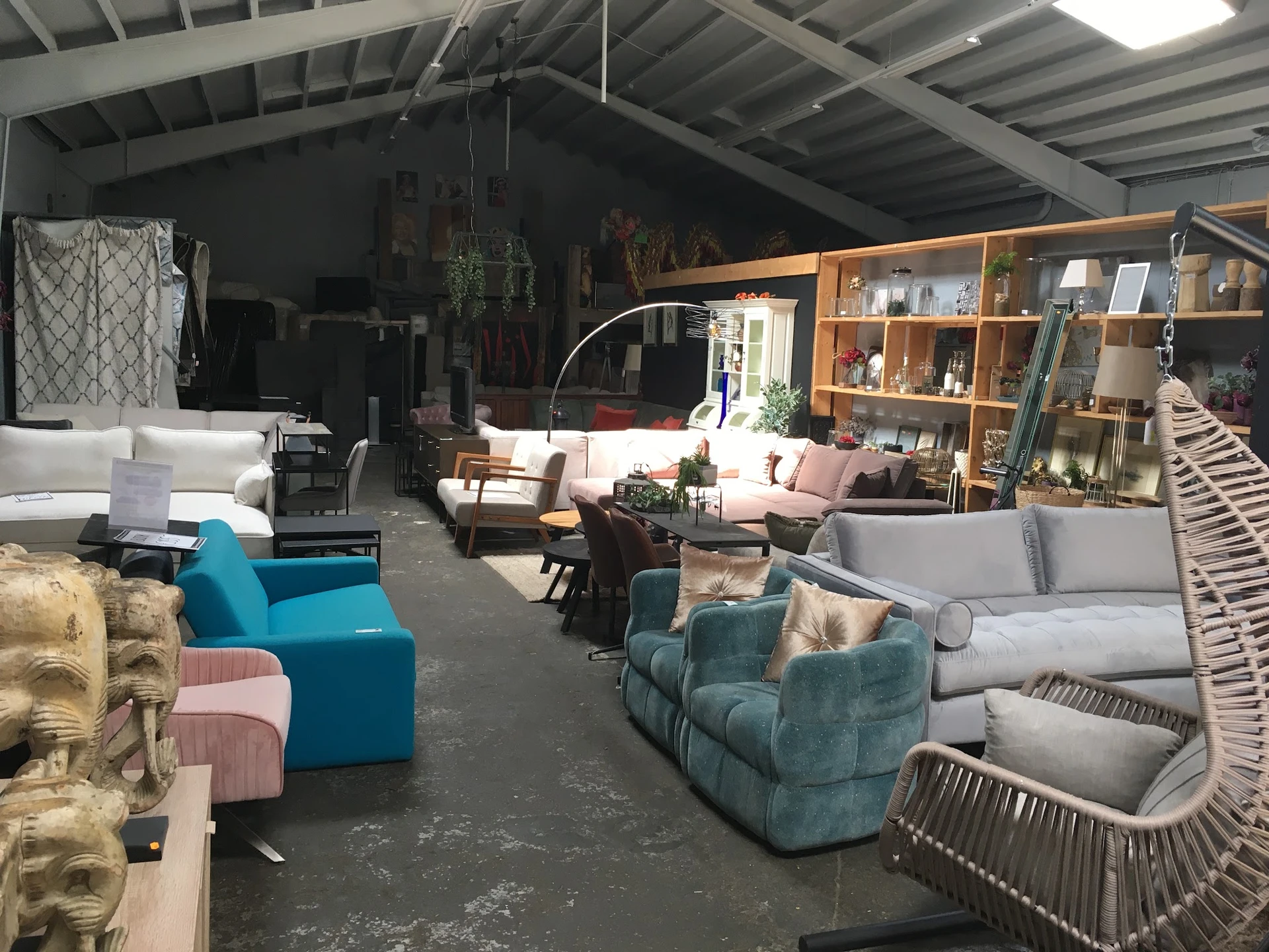 Ruime winkelruimte met diverse meubels: blauwe fauteuils, grijze banken, rotan stoelen en houten kasten tegen de muur