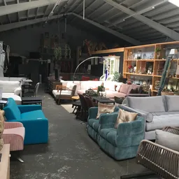 Ruime winkelruimte met diverse meubels: blauwe fauteuils, grijze banken, rotan stoelen en houten kasten tegen de muur