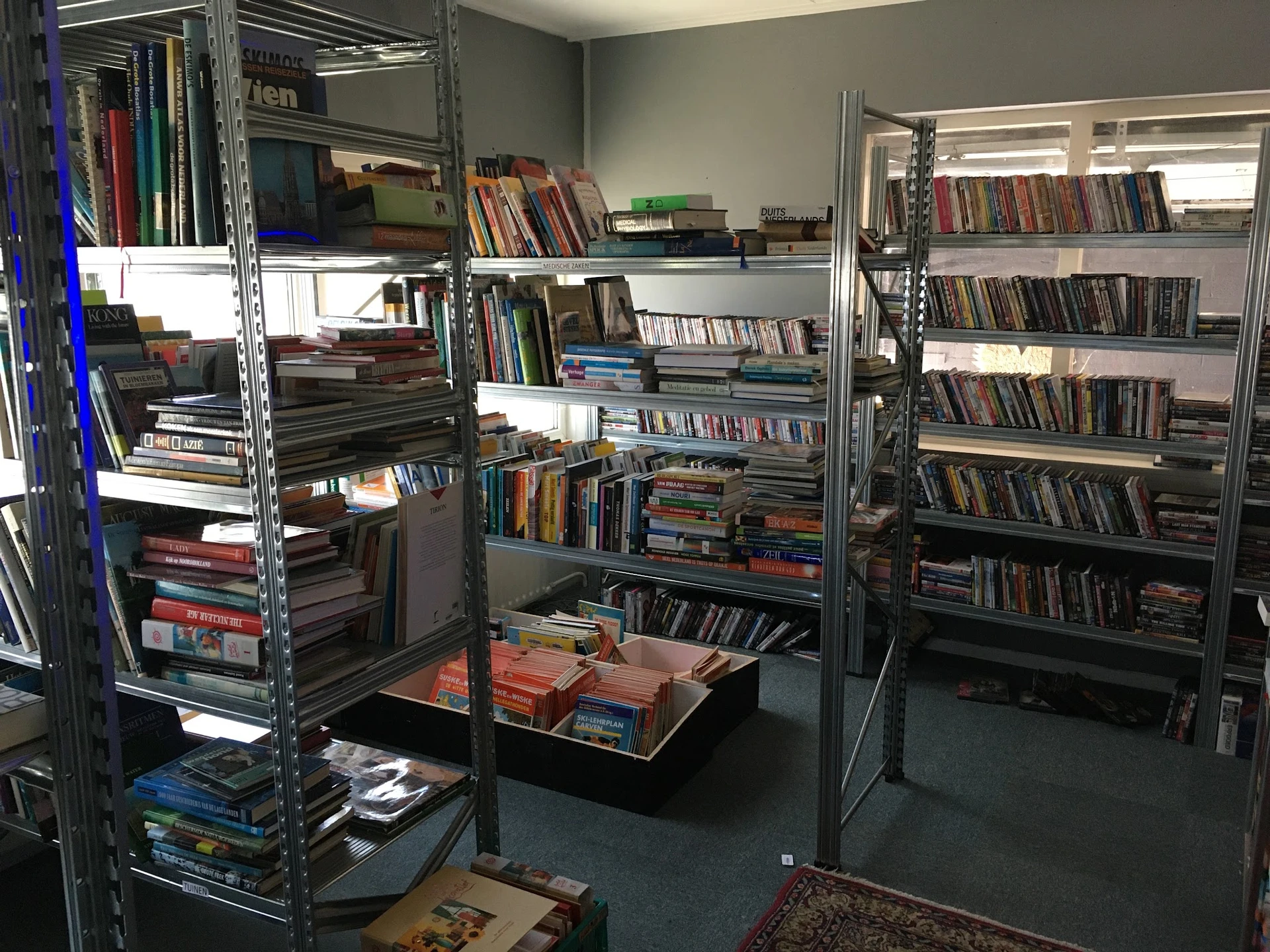 Winkelvloer met metalen stellingen vol dvd's, cd's en boeken, met dozen op de vloer