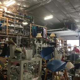 Binnenaanzicht van kringloopwinkel met stellingen, kleding, meubels en diverse spullen door elkaar