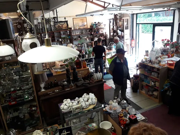Winkelvloer van kringloopwinkel met diverse artikelen, stellingen, lampen en huishoudspullen verspreid door de ruimte
