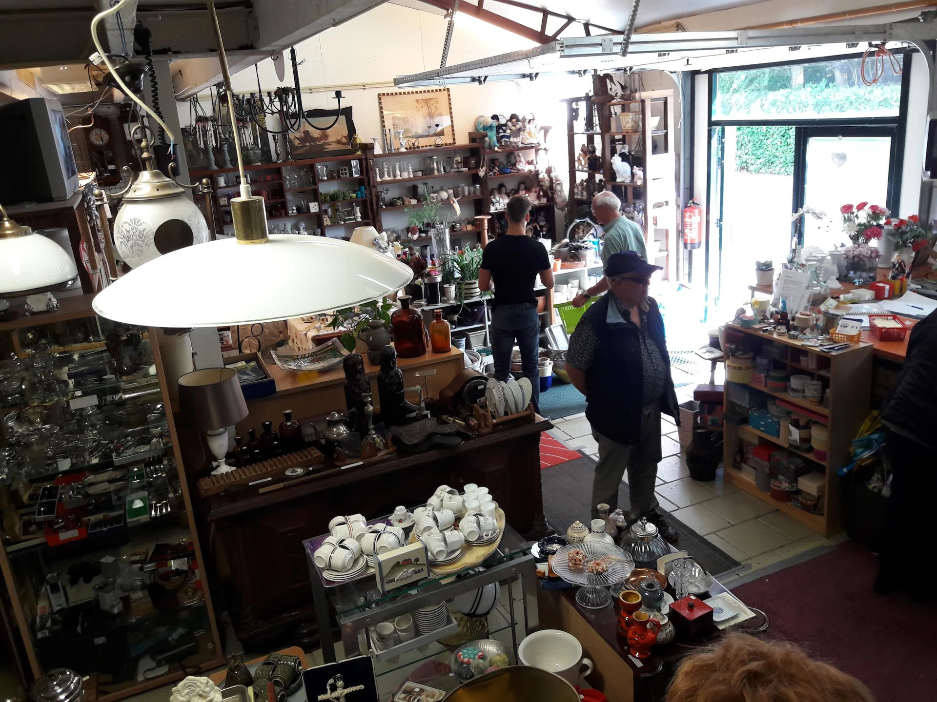 Winkelvloer van kringloopwinkel met diverse artikelen, stellingen, lampen en huishoudspullen verspreid door de ruimte