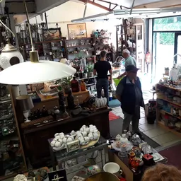 Winkelvloer van kringloopwinkel met diverse artikelen, stellingen, lampen en huishoudspullen verspreid door de ruimte