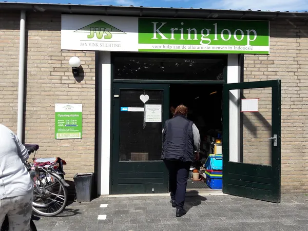 Winkel aan straat met groene deuren, witte en groene gevel met Kringloop-logo, fiets geparkeerd ernaast