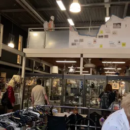 Winkelvloer van kringloopwinkel met glazen vitrines, bezoekers kijken naar uitgestalde spullen, goede belichting