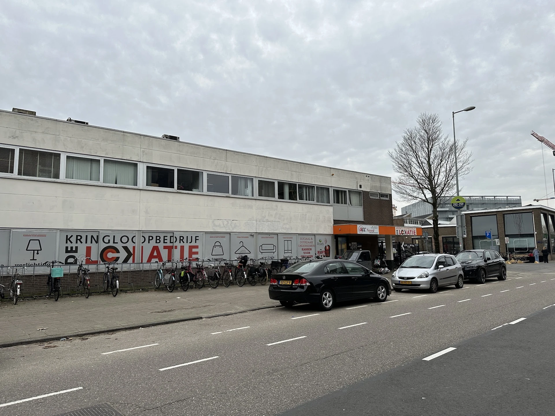 Voorgevel van kringloopwinkel met witte gevel, ramen en uithangtekst, parkeerplaats met auto's ervoor