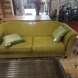 Geel Chesterfield-achtige tweepersoonsbank met groene sierkussens in de winkel