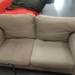 Tweepersoonsbank in beige stof met grijze rugkussens in een kringloopwinkel