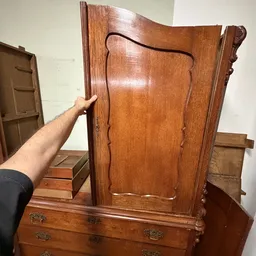 Close-up van een houten kast of meubeldeur met decoratief snijwerk, vastgehouden door een hand