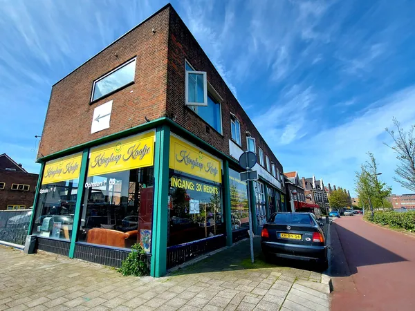 Gevel van kringloopwinkel met geel-groene pui en naam Kringloop Kaaltje, rode bakstenen gevelbouw onder blauwe hemel