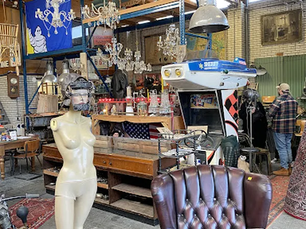 Winkelinterieur met diverse meubels, decoratie en vintage items, waaronder een witte mannequin, bruine leren stoel en een ret