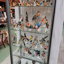 Glazen vitrinekast met verzameling van beeld- en speelgoedfiguren van vogels en andere dieren, geordend op twee niveaus.