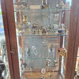 Glazen vitrinekast met antieke koperen en metalen huishoudartikelen en decoratieve voorwerpen op drie planken