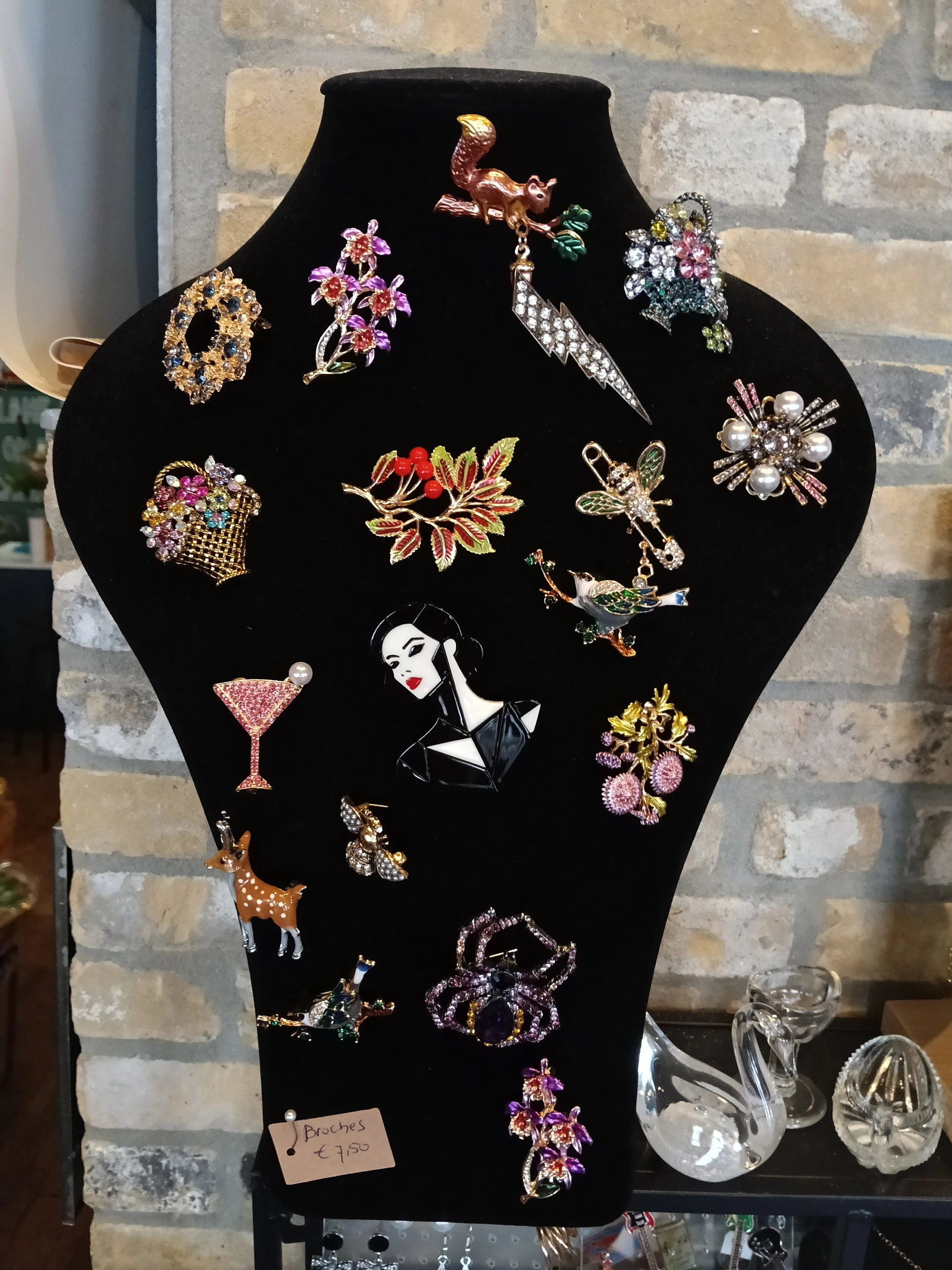 Verzameling vintage broche's en sieraden op een zwarte buste-display, waaronder bloemen, dieren en geometrische vormen in ver