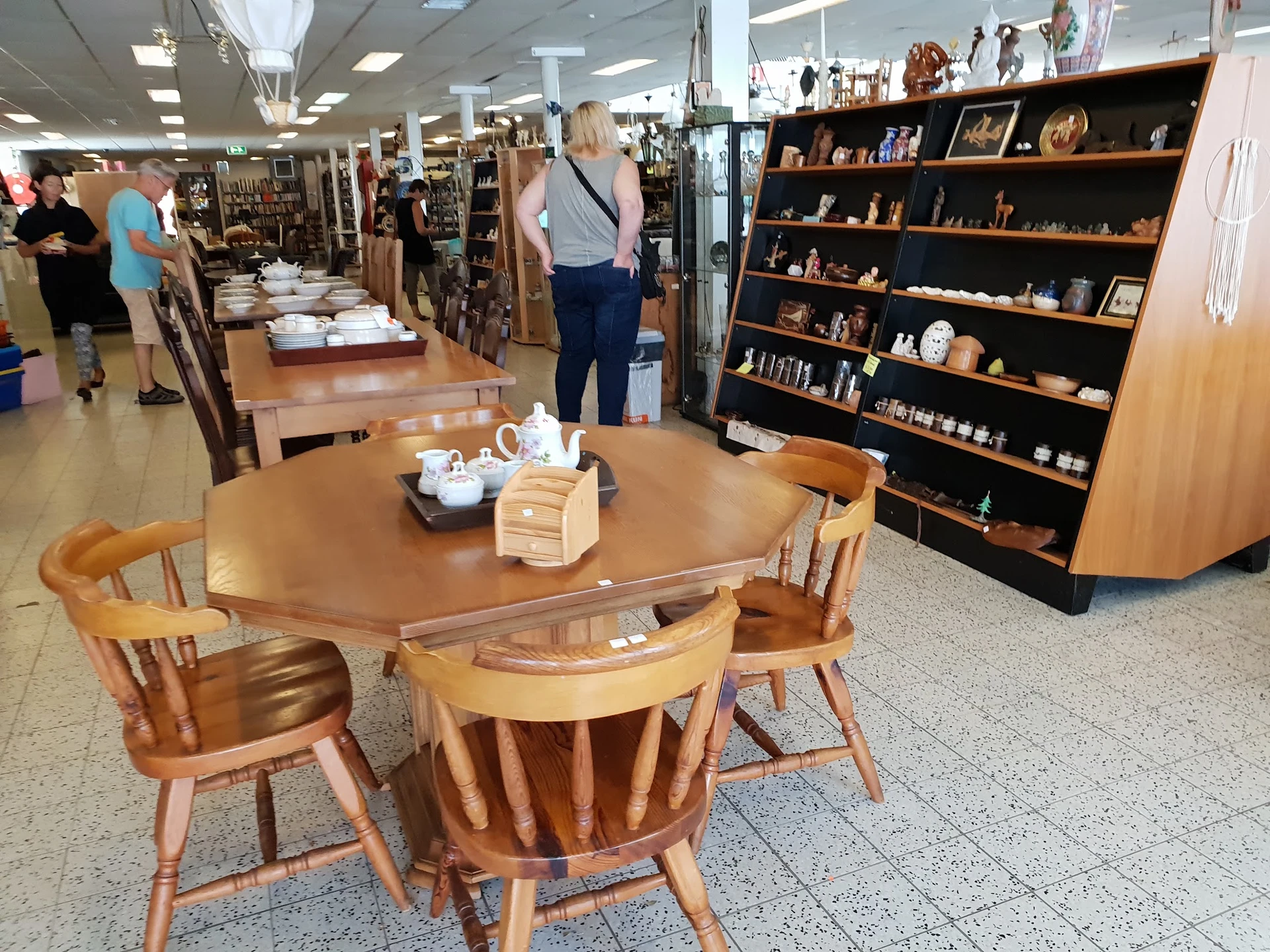 Winkelvloer met ronde houten eettafel met stoelen, zwarte boekenkast rechts, en andere meubels en spullen in de achtergrond