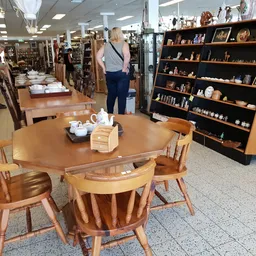 Winkelvloer met ronde houten eettafel met stoelen, zwarte boekenkast rechts, en andere meubels en spullen in de achtergrond