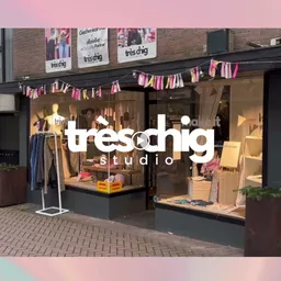 Winkelfront met glazen pui, winkelnaam 'treschhig studio' in witte letters, decoratieve slingers en uitgestalde kleding in et