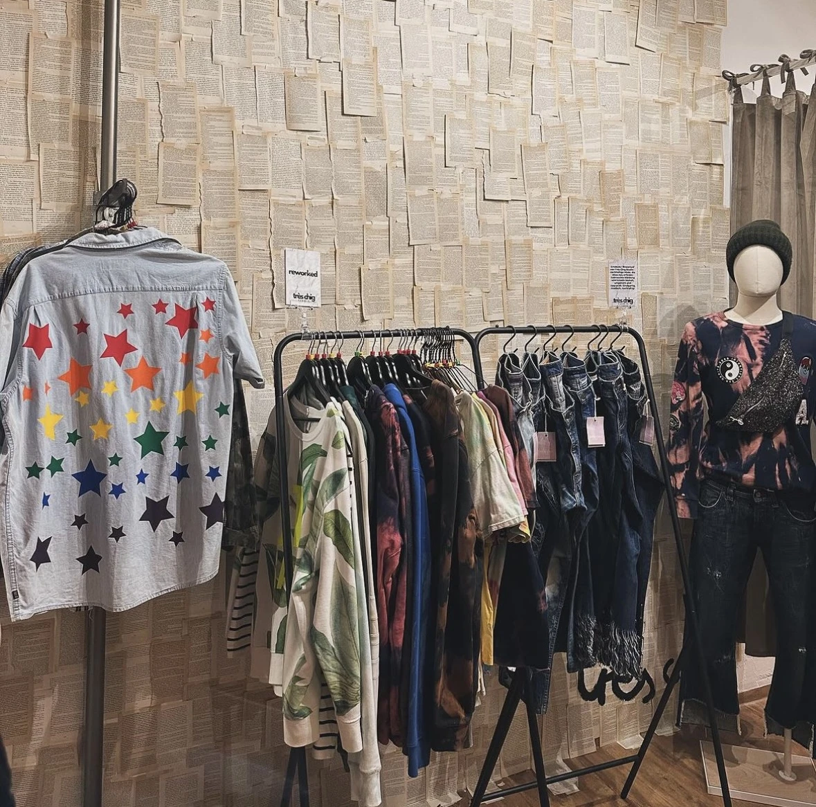 Rekken met tweedehands kleding, waaronder een grijze cardigan met gekleurde sterren en diverse donkere kledingstukken