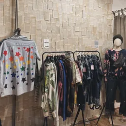 Rekken met tweedehands kleding, waaronder een grijze cardigan met gekleurde sterren en diverse donkere kledingstukken