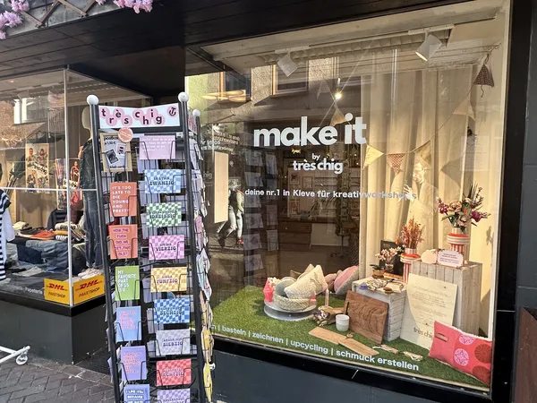 Winkelruit met 'make it tresdig' opschrift, etalage met decoratieve items en kunstbloemen, postcarddisplay links