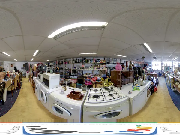 Overzicht van kringloopwinkel met huishoudelijke apparaten, kleding en diverse spullen op stellingen langs de wanden