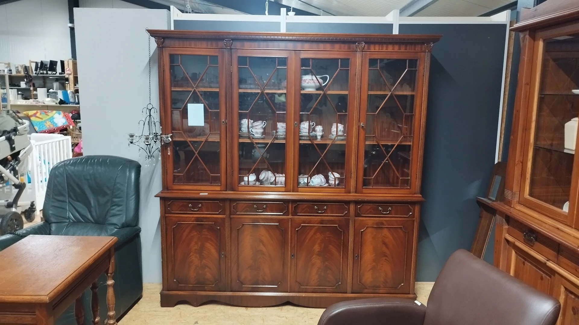 Houten vitrinekast met glas-in-lood deuren en onderkasten, gevuld met servies en decoratie