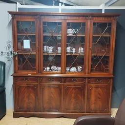 Houten vitrinekast met glas-in-lood deuren en onderkasten, gevuld met servies en decoratie